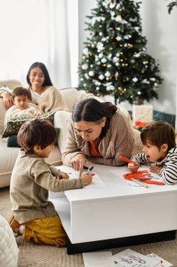Mutlu bir aile, güzel süslenmiş bir Noel ağacının yanında, samimi bir salonun etrafında toplanır ve festival sanatı yaratır..