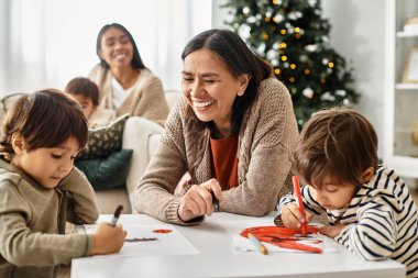 Mutlu bir aile Noel 'i birlikte kutlar, kahkahaları ve renkli sanat eserlerini rahat bir oturma odasında paylaşır..