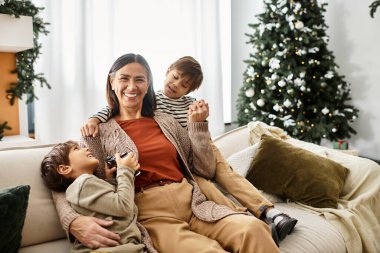 Asyalı bir aile, güzel dekore edilmiş bir Noel ağacının yanında birlikte vakit geçirmekten zevk alır, gülümsemelerini paylaşırlar..