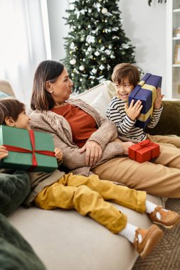 Mutlu bir aile Noel 'i kutlarken modern oturma odasındaki bir şenlik ağacının etrafına hediyeler açıyor..