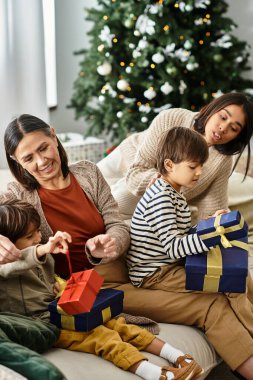 Neşeli bir aile, güzel dekore edilmiş bir Noel ağacının hediyelerini içeride açmaktan zevk alır..