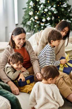 Neşeli bir aile modern bir salonda toplanıyor, Noel zamanı kahkahalar ve hediyeler paylaşıyorlar..