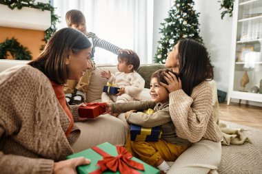 Neşeli bir aile Noel ağacının etrafında toplanıyor, hediyelerini değiş tokuş ediyor ve bayram ruhunu neşeyle kutluyor..