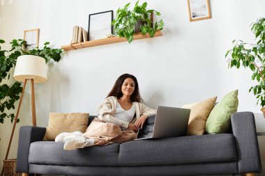 Kadın sakin bir anın tadını çıkarıyor. Laptopuyla çalışıyor. Etrafı yemyeşil bitkiler ve yumuşak yastıklarla çevrili..