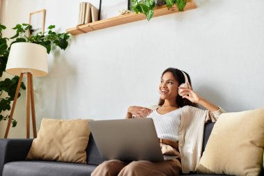 Kadın kanepede dinleniyor, dizüstü bilgisayarıyla meşgul ve neşeli müziğin tadını çıkarıyor..