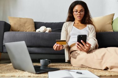 Gözlüklü bir kadın oturma odasında yerde otururken online alışveriş yapmaktan hoşlanır..
