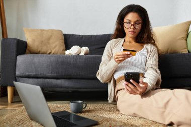 Konforlu bir oturma odasında, bir kadın telefon ve kredi kartıyla online alışveriş yapıyor..