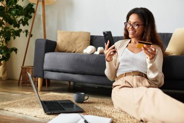 Neşeli bir kadın dizüstü bilgisayarı ve akıllı telefonuyla internette mutlu bir şekilde alışveriş yapıyor..