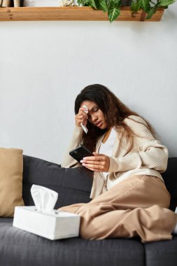 Bir kadın koltukta dinlenirken telefonunu kullanırken düşünceli ve duygusal görünür..