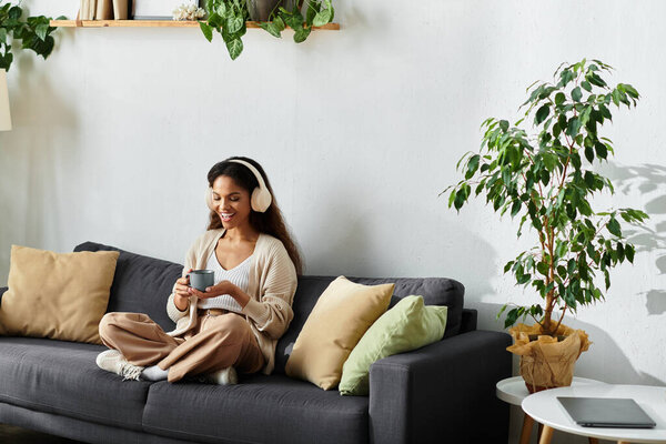 A cheerful woman relaxes on a comfortable couch, sipping from a warm cup in a cozy setting.