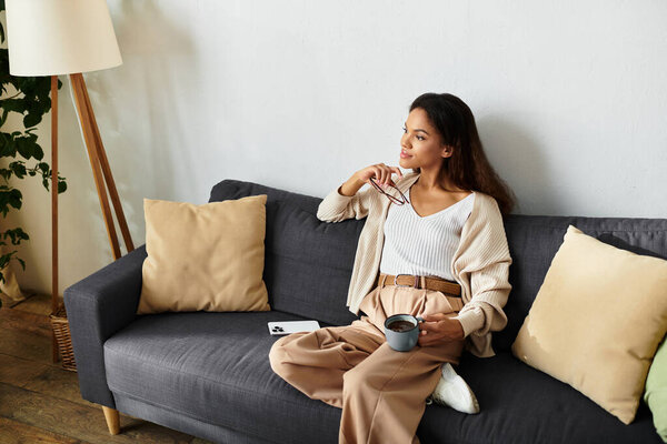 The woman relaxes on a comfortable sofa while sipping coffee and reflecting on her day.