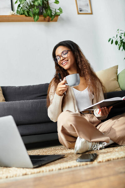 Улыбающаяся женщина расслабляется на полу с горячим напитком и открытой книгой в руке.