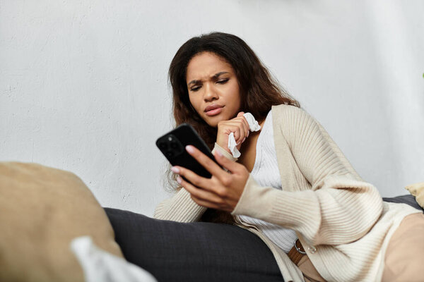 A young woman rests on a couch, intently gazing at her smartphone with a worried expression.