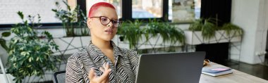 A bald woman with vibrant hair color shares ideas in a stylish work environment. clipart