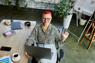 Şık bir iş yerinde laptopunu kullanan, kızıl saçlı, kendine güvenen, kel bir kadın..