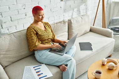 A bald woman engages in creative work, focused on her laptop in a cozy space. clipart