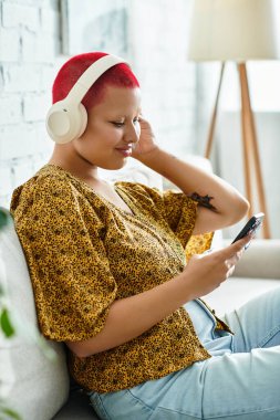 Canlı kızıl saçlı kel bir kadın evde dinlenirken dikkatle müzik dinliyor..