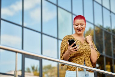 Neşeli, kel bir kadın, açık havada güneşli bir günü kucaklayarak akıllı telefonuyla meşgul olur..