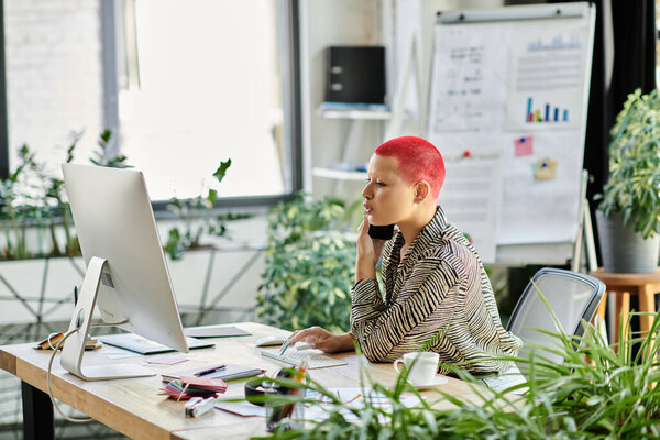 A bald woman chats on the phone at her desk, surrounded by greenery.