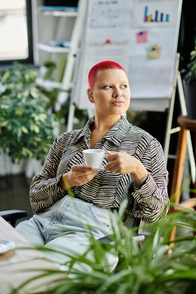 Лысая женщина с яркими рыжими волосами отражает, наслаждаясь кофе в современном рабочем пространстве.