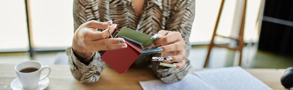 Красивая лысая женщина рассматривает яркие образцы ткани, когда она потягивает кофе в ярком пространстве..