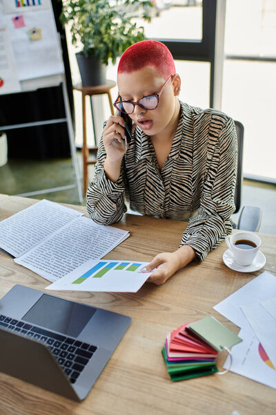 A committed woman with a stylish bald look reviews charts as she talks on the phone.