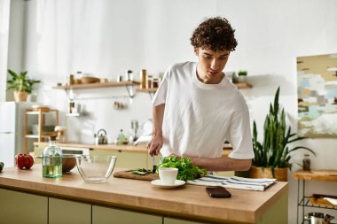 Yakışıklı genç bir adam taze sebzeleri doğruyor, modern mutfağında sağlıklı beslenerek..