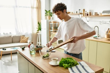 Yakışıklı genç bir adam, çağdaş bir mutfakta sağlıklı bir yaşam tarzını benimseyen yeşillikleri bir kaseye ustalıkla atıyor..