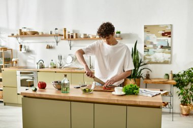 A handsome young man skillfully slices vegetables while making a vibrant salad in his contemporary kitchen. clipart