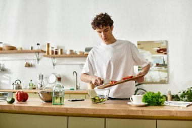 Yakışıklı bir genç adam çağdaş mutfağında canlı bir salata yaparken ustaca sebze doğruyor..