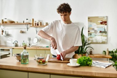 Şık bir genç adam şık bir mutfakta eğlenirken canlı bir salata yapmak için sebze doğruyor..