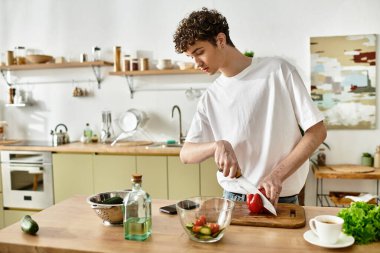 Kıvırcık saçlı yakışıklı bir genç adam zevkle şık mutfağında sağlıklı bir salata yapıyor..