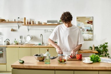 Şık bir mutfakta, yakışıklı genç bir adam sağlıklı yaşam ve mutfak yaratıcılığını kucaklayan canlı bir salata hazırlar..