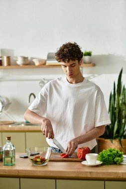 Parlak bir mutfakta, yakışıklı genç bir adam lezzetli bir salata yapmak için taze sebzeleri ustalıkla doğruyor..