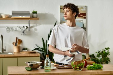 Şık bir mutfakta, yakışıklı genç bir adam düşünceli bir şekilde taze bir salata hazırlıyor, sağlıklı bir hayatı kucaklıyor..