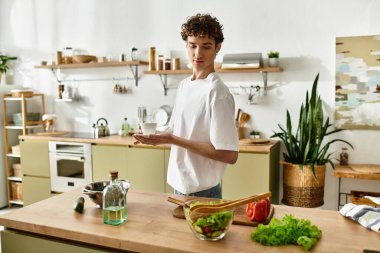 Yakışıklı genç bir adam şık bir mutfakta canlı bir salata pişiriyor, sağlıklı beslenme alışkanlıklarını kucaklıyor..