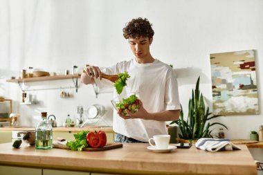 Yakışıklı bir genç adam şık bir mutfakta, sağlıklı bir yaşam tarzını kucaklayan taze malzemeleri ustalıkla karıştırıyor..