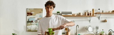 A handsome young man creates a salad, embodying healthy living in a sleek kitchen setting. clipart