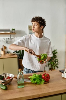 Yakışıklı genç bir adam canlı bir salata yapmaktan hoşlanıyor, modern mutfağında sağlıklı yemek yapmaktan zevk alıyor..