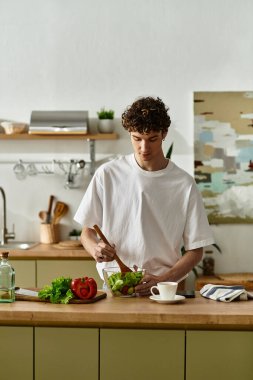 Yakışıklı genç bir adam, çağdaş bir mutfakta sağlıklı bir salata yapıyor, hayat dolu bir yaşam tarzını kucaklıyor..