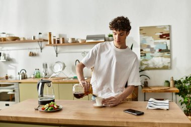 Yakışıklı genç adam kahvaltının tadını çıkarırken taze demlenmiş kahveyi bir fincana doldurur..