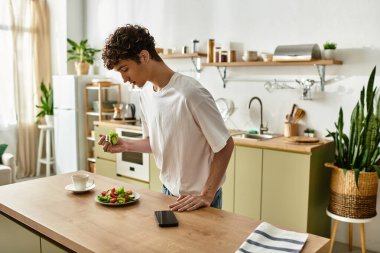 Şık bir mutfakta, yakışıklı genç bir adam boş zamanlarında renkli bir salata yiyor..