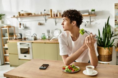 Yakışıklı bir genç adam şık bir mutfakta dinlenirken enerjik bir salatanın tadını çıkartıyor..