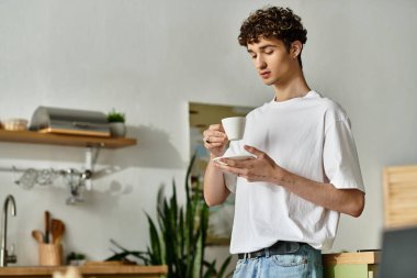 Sıcak bir mutfakta genç bir adam, sakin bir sabah havasına dalmış kahvesinin tadını çıkarıyor..