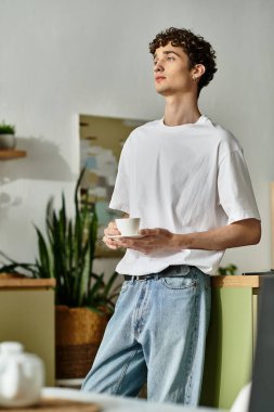 Modern bir mutfakta duran şık bir genç adam kahvesini yudumluyor ve sakin atmosferin tadını çıkarıyor..