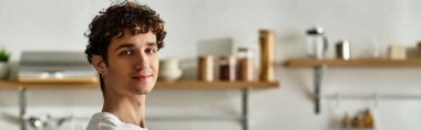 Modern bir mutfakta, kıvırcık saçlı, neşeli ve yaratıcı bir genç adam....