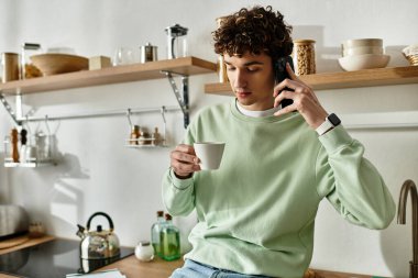 Şık bir mutfakta, yakışıklı genç bir adam telefonda konuşurken içkinin tadını çıkarıyor, gevşek bir cazibe yayıyor..