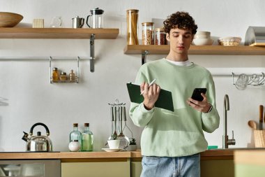 Şık bir mutfakta, kıvırcık saçlı genç bir adam telefonundaki tarifleri incelerken notlar alır..