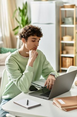 Kıvırcık saçlı yakışıklı genç bir adam, yeşilliklerle çevrili modern ev ofisinde düşünceli bir şekilde işe girişiyor..