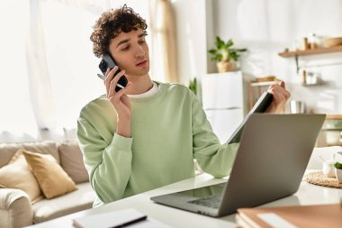 Genç bir adam, modern ve güneşli bir yaşam alanında telefonunu ve laptopunu kullanarak uzak bir işe girişiyor..